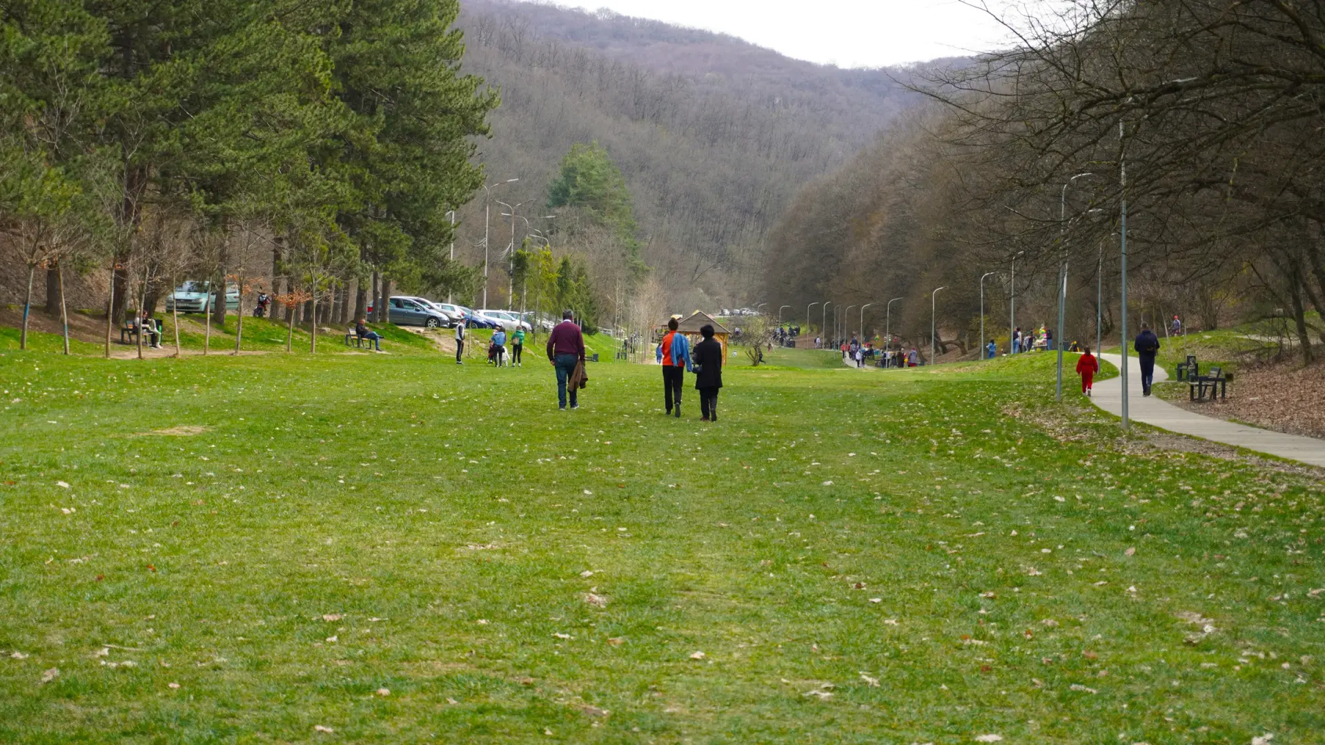 Walkers on the main meadow at Germia Park, with forested hills rising on the edge of Prishtina