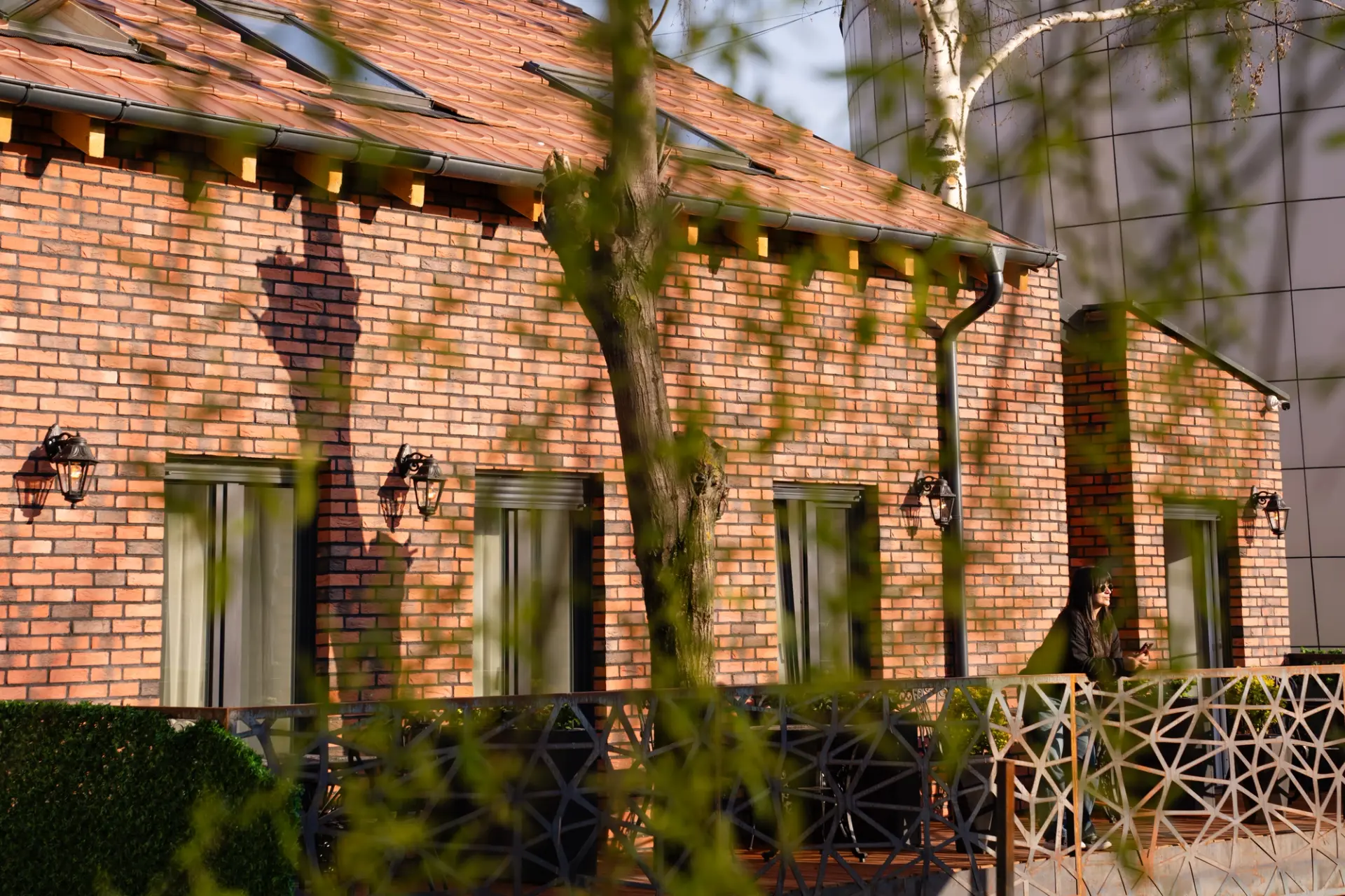 The red brick facade of ZOE Hotel in central Prishtina, with balconies and wall lanterns seen through spring branches